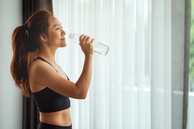 Uma linda mulher asiática bebendo água de uma garrafa de plástico enquanto se exercita