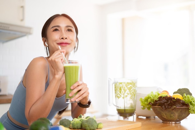 Uma linda mulher asiática está desfrutando de seu saudável smoothie verde na cozinha após o treino