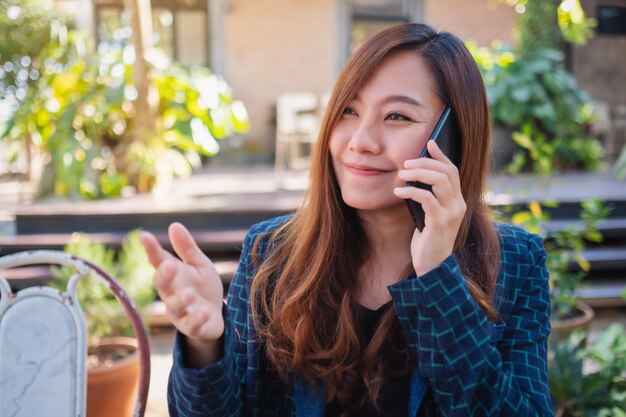 Uma linda mulher asiática falando no celular com uma cara sorridente ao ar livre