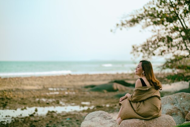 Uma linda mulher asiática gosta de sentar-se na rocha à beira-mar