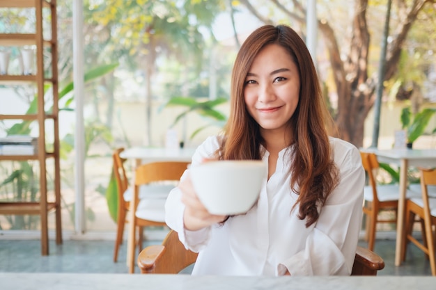 Uma linda mulher asiática segurando e dando uma xícara de café sentindo-se bem no café