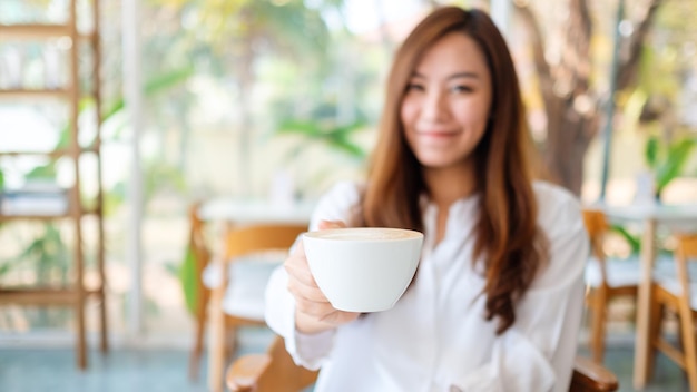 Uma linda mulher asiática segurando e dando uma xícara de café sentindo-se bem no café