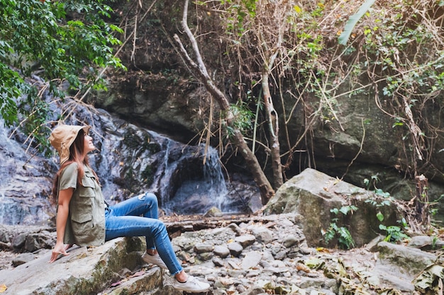 Uma linda mulher asiática sentada na rocha em frente à cachoeira