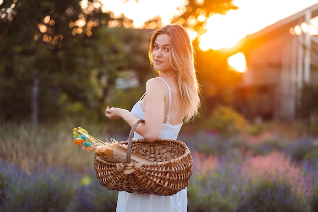 Uma linda mulher caucasiana de vestido branco caminha no prado de lavanda à noite na hora dourada