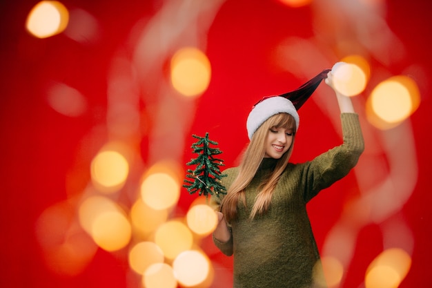 Foto uma linda mulher com um chapéu de papai noel segura uma pequena árvore de natal nas mãos. conceito de ano novo