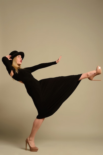 Uma linda mulher com um chapéu preto e um vestido de noite com salto leva um vento forte
