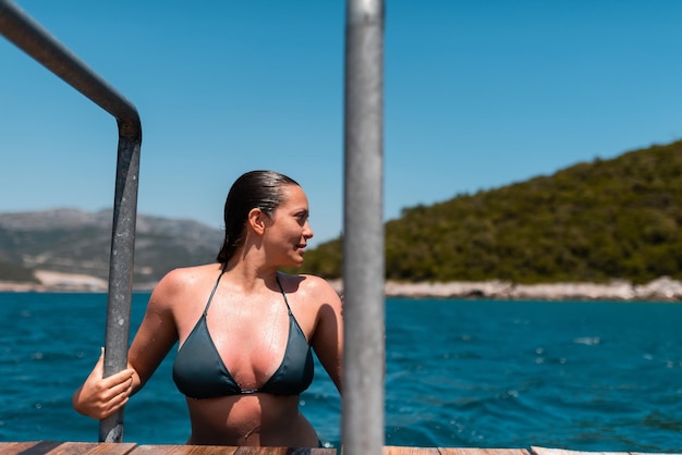 Uma linda mulher com um corpo sexy em um biquíni verde em uma praia tropical emerge do mar pelas escadas