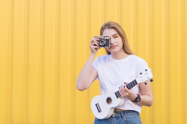 Uma linda mulher com um ukulele na mão faz a foto na câmera retro.