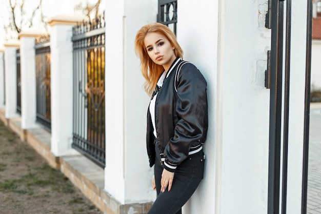 Uma linda mulher com uma jaqueta elegante e jeans preto perto da cerca