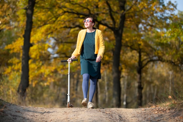 Uma linda mulher de meia idade caminha com uma scooter no outono