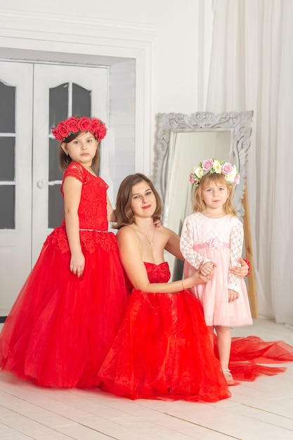 Uma linda mulher em um longo vestido rosa em um salão com flores é fotografada com suas filhas que têm coroas de flores em suas cabeças As meninas são fofas Primavera PHOTOSESSION Família