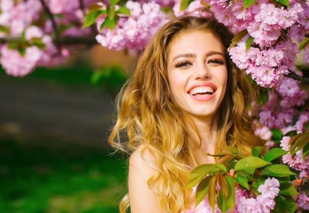 Uma linda mulher em um parque de flor rosa. Jovem feliz com um sorriso no rosto, aproveite a primavera