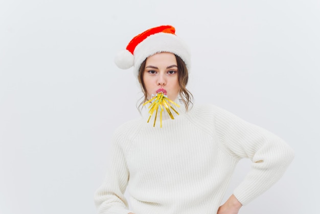 Foto uma linda mulher em um suéter e chapéu de papai noel está soprando uma música festiva rindo e olhando para a câmera