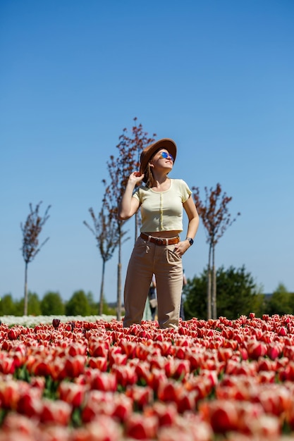 Uma linda mulher esbelta com um chapéu fica em um campo florescente de tulipas Tempo de primavera