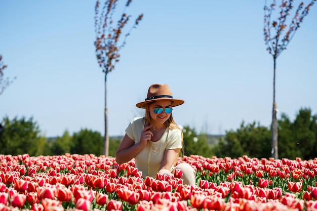 Uma linda mulher esbelta com um chapéu fica em um campo florescente de tulipas Tempo de primavera