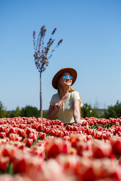 Uma linda mulher esguia com um chapéu está em um campo de tulipas florescendo. Tempo de primavera