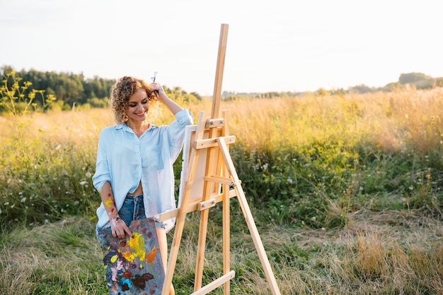 Uma linda mulher está pintando. Sessão ao ar livre. Mulher bonita tira uma foto ao pôr do sol. menina artista