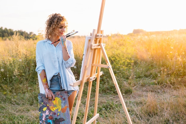 Foto uma linda mulher está pintando. sessão ao ar livre. mulher bonita tira uma foto ao pôr do sol. menina artista