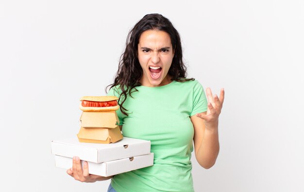 Uma linda mulher hispânica parecendo zangada, irritada e frustrada segurando caixas de fast food para levar