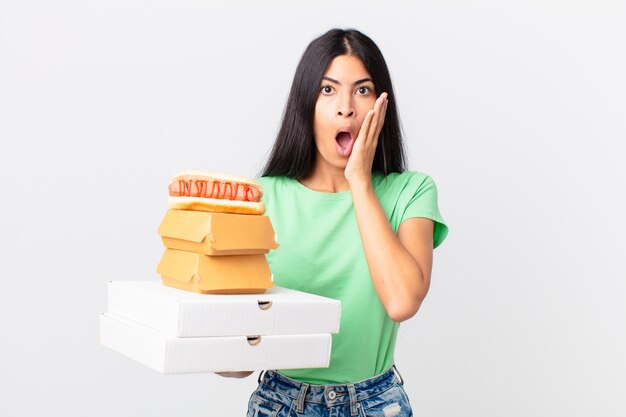 Uma linda mulher hispânica se sentindo chocada e com medo, segurando caixas de comida rápida