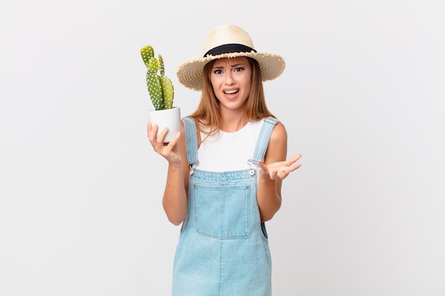 Uma linda mulher parecendo desesperada, frustrada e estressada segurando uma planta decorativa de cacto