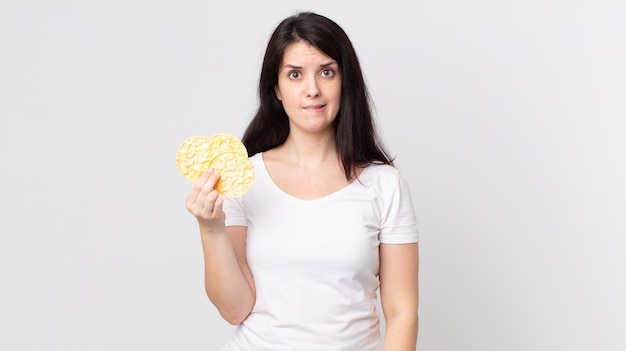 Uma linda mulher parecendo perplexa e confusa segurando um bolo de arroz diet