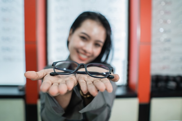 Uma linda mulher posa segurando os óculos no fundo de uma vitrine de óculos em uma clínica de olhos