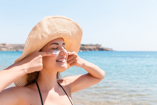 Uma linda mulher protege a pele do rosto com protetor solar na praia.