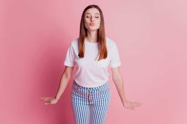 Uma linda mulher romântica e sonhadora dando um beijo no ar com os lábios na parede rosa