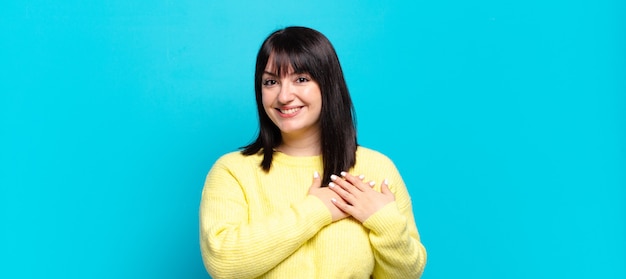 Uma linda mulher se sentindo romântica, feliz e apaixonada, sorrindo alegremente e segurando as mãos perto do coração