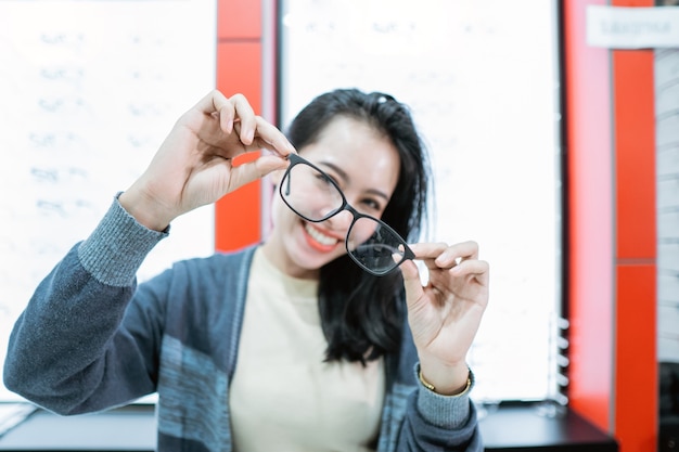 Uma linda mulher segurando uma amostra de óculos em uma clínica de olhos contra o fundo de uma vitrine