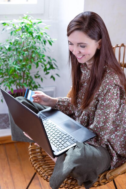 Uma linda mulher sorridente com cabelo comprido sentado na cadeira segurando um laptop e olhando onlineshope