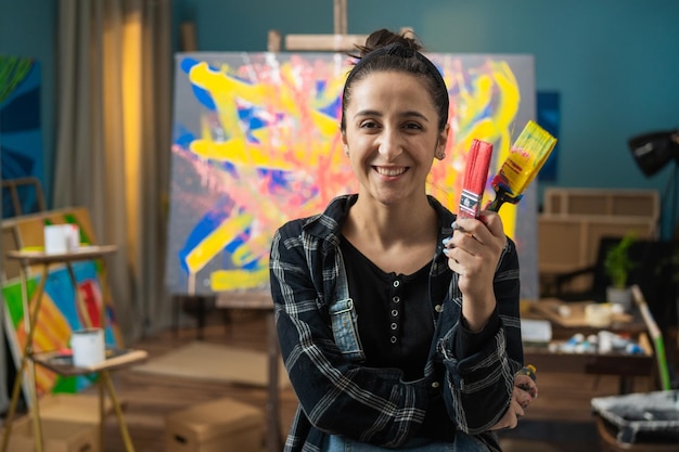 Uma linda mulher sorridente fica em um estúdio de pintura contra um cavalete com uma tela