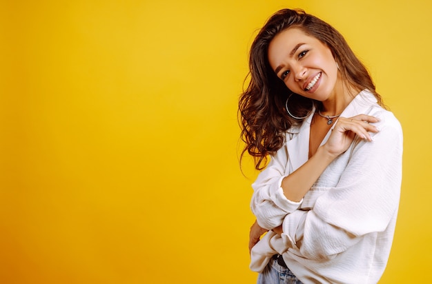 Uma linda mulher usa uma camisa branca e calça jeans.