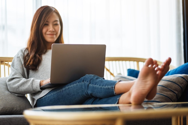 Uma linda mulher usando e trabalhando em um laptop enquanto estava deitada em um sofá em casa