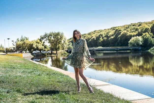 Uma linda mulher vestida estava de pé à beira do lago, relaxando com a natureza e fazendo poses para a câmera