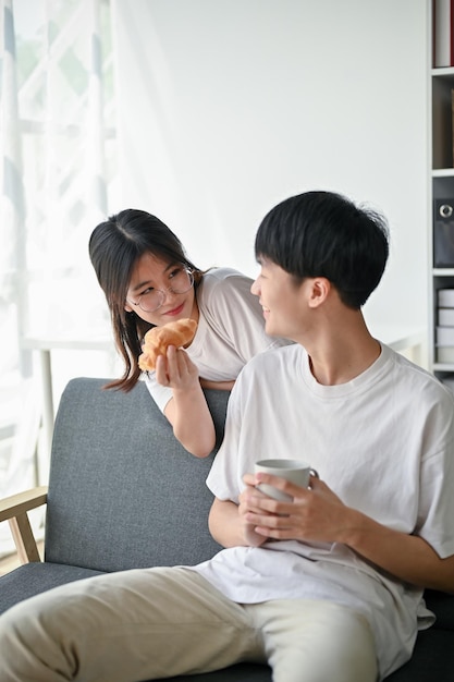 Uma linda namorada asiática brincando e alimentando um delicioso croissant para o namorado