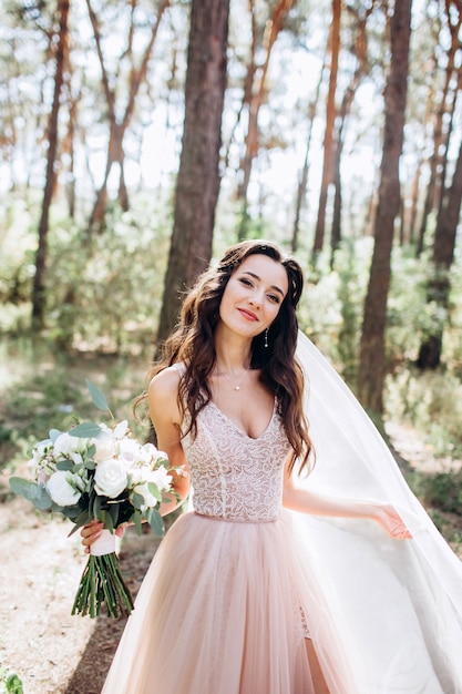 Uma linda noiva em um vestido rosa delicado ao ar livre. A garota está segurando um buquê