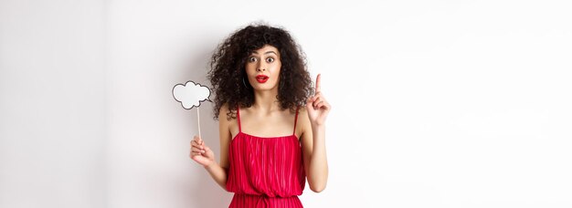 Foto uma linda senhora caucasiana de vestido vermelho segurando uma nuvem de comentários e levantando o dedo lançando uma ideia e