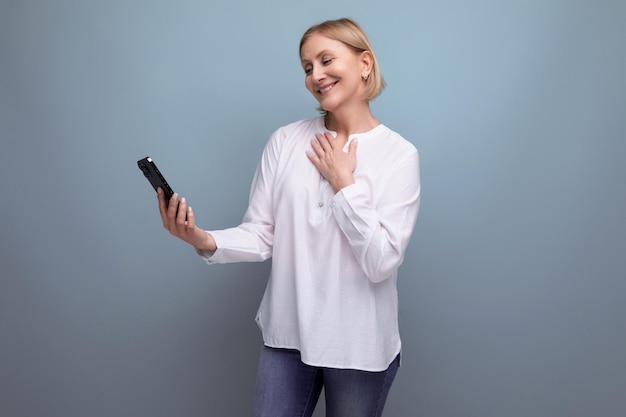 Uma loira esbelta e pensativa de meia-idade em uma blusa branca domina o gadget do smartphone