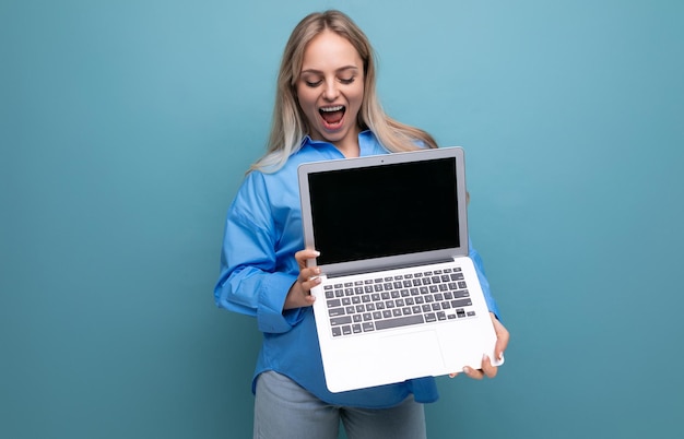 Uma loira feliz e sortuda se alegra com um laptop em suas mãos com um espaço vazio para uma página da web em um