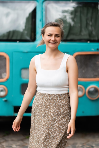 Uma loira linda sorridente está ao lado de um ônibus escolar antigo e olhando para a câmera