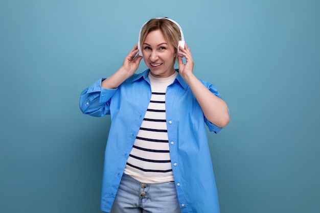 Uma loira sorridente caucasiana vestida com um suéter listrado e uma camisa casual ouve música no