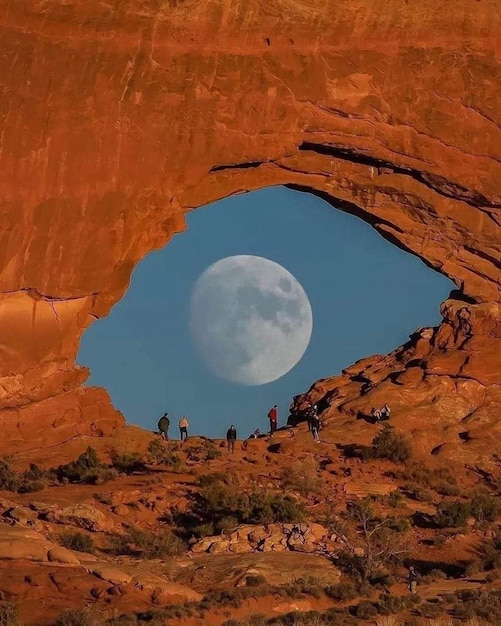 Foto uma lua cheia é visível através de um buraco em uma formação rochosa.