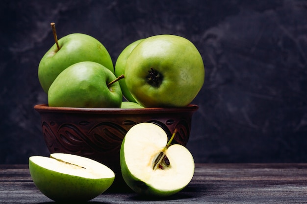 Uma maçã verde meio cortada ao lado de uma tigela cheia de maçãs