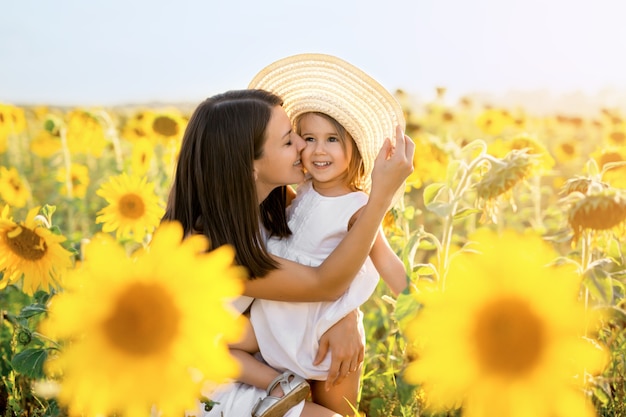 Uma mãe abraça e beija carinhosamente sua filha ao pôr do sol em um campo de girassóis