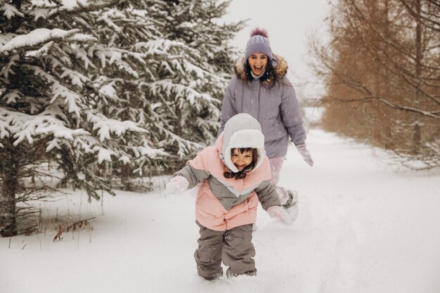 Uma mãe alegre alcança sua filha, que corre pela neve na floresta. passeios de inverno