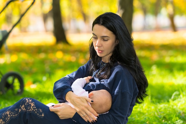 Uma mãe amamentando discretamente seu bebê em um parque externo bem iluminado.