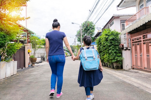 Uma mãe asiática está segurando sua filha para levar à escola pela filha carregando uma mochila de volta ao conceito de escola