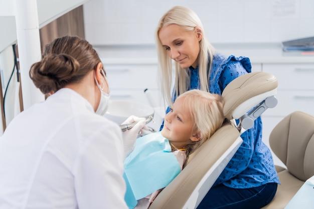 Uma mãe assistindo a um dentista cuidando dos dentes de sua filha.